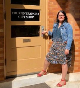 Rosina Saqib stands in front of the door to Evergreen's Gift Shop, with one hand on the doorknob. 