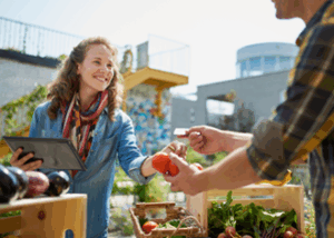 woman at a farmer's market in a city environment accepting a credit card in exchange for tomatoes