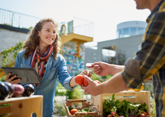 woman at a farmer's market in a city environment accepting a credit card in exchange for tomatoes