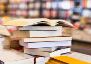 stack of books on a table with a background of shelves full of books