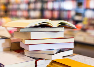 stack of books on a table with a background of shelves full of books
