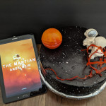 Cake decorated with astronauts in space next to Samsung tablet with "The Martian" book cover